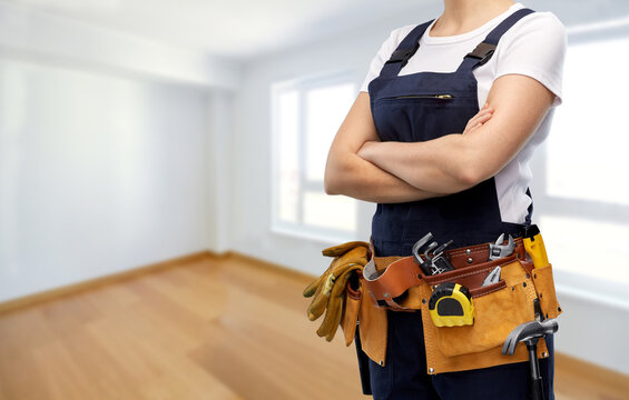 repair, construction and building concept - woman or builder with working tools on belt over empty room at new home background
