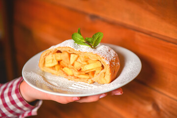Waiter serving piece of apple strudel with powdered sugar on a white plate. Restaurant service.