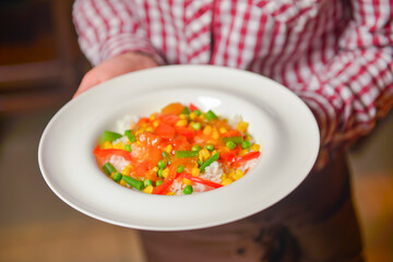 Waiter serving rice with red, green and yellow pepper, tomatoes, red onion, celery. Restaurant service.