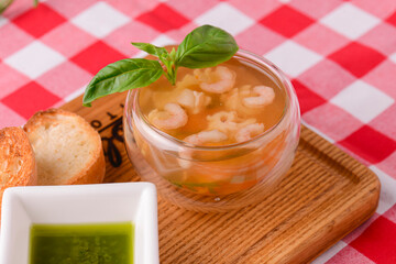 Hot and sour soup with shrimps and seafood served in a small glass bowl on rustic wooden board.