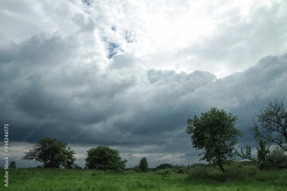 Wall mural thunderous epic clouds in a field near the old garden. stock photo background with heaven.