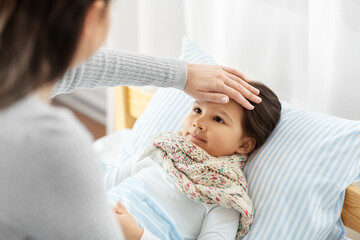 family, health and people concept - mother measuring temperature of sick daughter lying in bed at home with hand