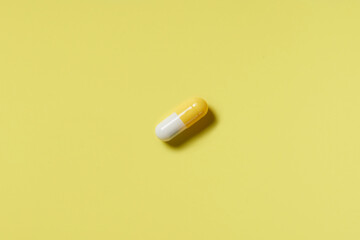 Yellow and white pill on a yellow background. Hard light. Paper background
