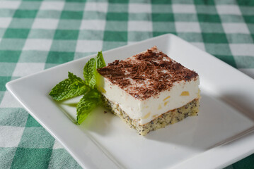 Traditional Italian dessert tiramisu served on a white plate with a mint leaf in a restaurant. Italian cuisine, dessert.