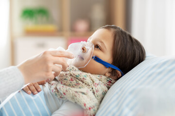 family, health and medicine concept - mother and sick little daughter lying in bed with oxygen mask or nebulizer at home