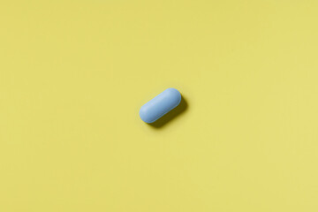 Blue pill on a yellow background. Hard light. Paper background