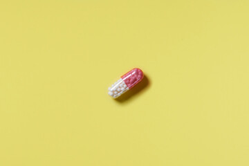 Pink and white pill on a yellow background. Hard light. Paper background