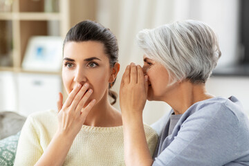 family, generation and people concept - senior mother whispering secret to adult daughter at home - obrazy, fototapety, plakaty