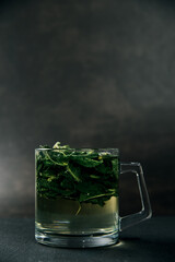 Close up of boiled mint leaves in a glass mug on a dark background. Copy space