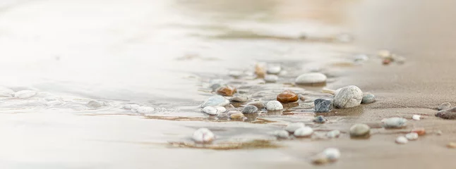 Selbstklebende Fototapete Steine​ im Sand Eine Nahaufnahme von glatt polierten bunten Steinen, die am Strand an Land gespült wurden.