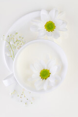 White set cup and saucer in a milk bath with white flowers.