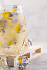 Champagne cocktail with ice and flowers on a light gray background.