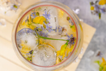 Champagne cocktail with ice and flowers on a light gray background.