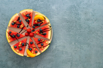 Colorful juicy watermelon pizza topped with berries, nuts, and chocolate sauce. Top view, copy space.