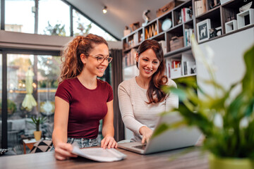 Home portrait of a two smiling women looking at laptop.