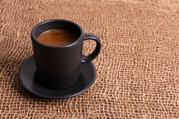 Single grey cup of black coffee with foam on jute burlap sackcloth. High angle, sack copy space. Coffee shop, morning, agriculture, traditional roast concept