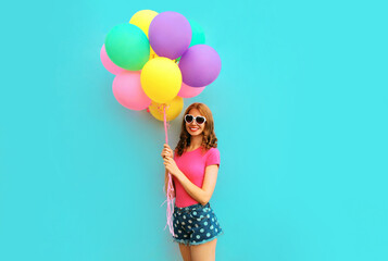 Happy smiling young woman with bunch of balloons having fun wearing a shorts and pink t-shirt on blue wall background