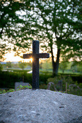 A metal cross on a rocky surface on a graveyard with the sunlight shining behind it, giving a sense of hope
