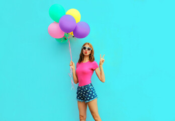 Fototapeta na wymiar Attractive young woman with bunch of colorful balloons having fun on blue wall background