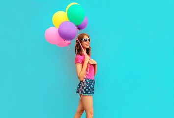 Happy smiling young woman with bunch of balloons having fun wearing a shorts and pink t-shirt on blue wall background