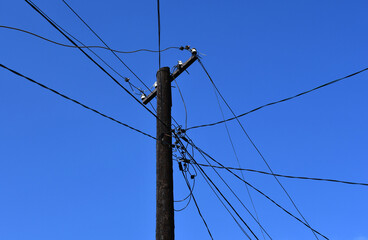 A black wooden pole covered with fuel oil, to which a lot of wires stretch.