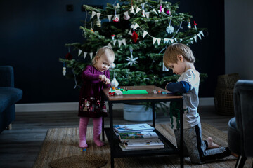 Festive interior, Christmas tree. Brother and sister play Bricks near the tree.