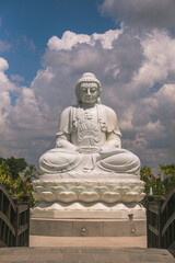 Obraz premium the solemn white statue of Buddha sitting on a high pedestal behind is a clear blue sky with white clouds