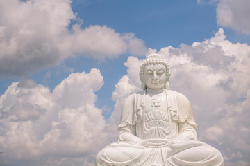 Obraz premium the solemn white statue of Buddha sitting on a high pedestal behind is a clear blue sky with white clouds