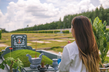 An unidentified woman is lighting incense, prostrating in front of an unidentified tomb in the cemetery. Concept of spiritual and religious