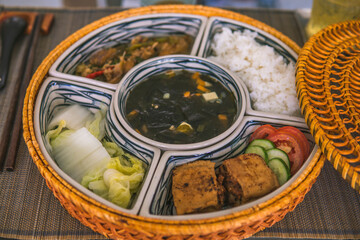 rice bowl with rattan, inside is traditional Vietnamese lunch, rice, soup, salty food. The scene is frugal and peaceful.