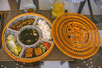 rice bowl with rattan, inside is traditional Vietnamese lunch, rice, soup, salty food. The scene is frugal and peaceful.