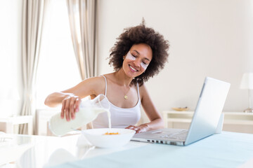 A young woman prepares a low-calorie breakfast on a prescription while looking at her laptop....
