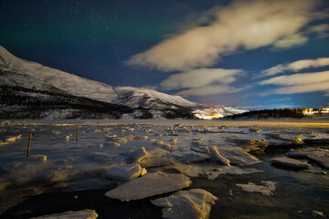 Eisschollen auf einem See in Norwegen im Hintergrund Wolken mit Polarlichter