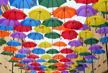Fototapeta na wymiar Colorful umbrellas strung up between the shops, protect shoppers from any rain, above St Lawrence Street ,SouthGate, Bath, England.