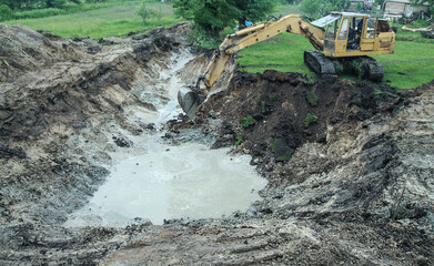 An excavator digs a large trench for building a house. A tractor digs a large lake that is already gaining water. Stock background for design