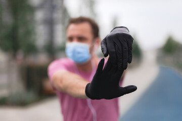 Sportsman with medical mask and gloves, smartphone and earbuds working out, jogging in urban surroundings.