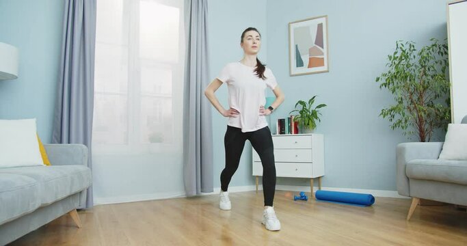 Middle plan of beautiful fit woman doing fitness workout and lunges exercises for healthy lifestyle and strong legs muscules in living room at home. Sport and fitness. Training, workout and wellness.