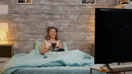 Obraz premium Zoom in shot of beautiful woman in pajamas at night watching tv with her dog.
