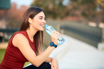 Thirsty young sporty woman making pause and drinking water during exerising.