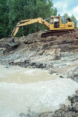 An excavator digs a large trench for building a house. A tractor digs a large lake that is already gaining water. Stock background for design