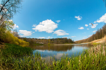 Spring panorama of a forest lake against a background of blue sky and distant mountains