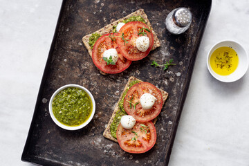 Mozzarella cheese, tomatoes and  pesto bruschetta on light marble background, top view. Pesto and sandwiches
