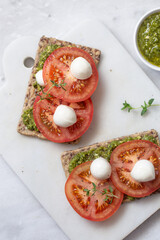 Mozzarella cheese, tomatoes and  pesto bruschetta on light marble background, top view. Pesto and sandwiches