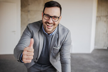 Young smiling businessman showing thumbs up. Building in construction process interior.