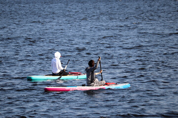 Sup surfing, two girls with paddles riding on a boards in a sea. Paddleboarding in summer