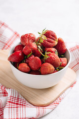 Closeup fresh garden strawberry in a plate on a wooden kitchen board with a beautiful napkin and serving, wholesome food and vitamins, diet. Vertical photo with place for text.