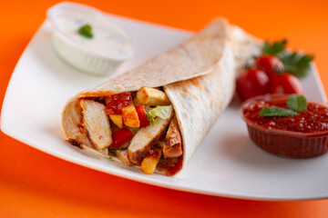 Grilled chicken in sandwich from fresh pita bread with onion and greens on  white plate