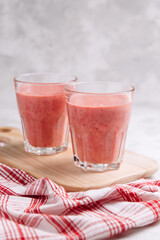 Strawberry smoothie in glasses on a wooden board with a beautiful serving of red napkin on a light background. Still life with place for text.