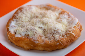 Traditional Transylvanian hungarian pastry, deep fried dough langos close up on restaurant table with cheese, sour cream and garlic.