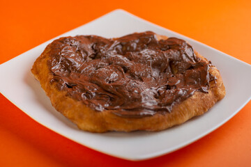 Traditional Transylvanian hungarian pastry, deep fried dough langos with cacao cream chocolate close up on white plate
